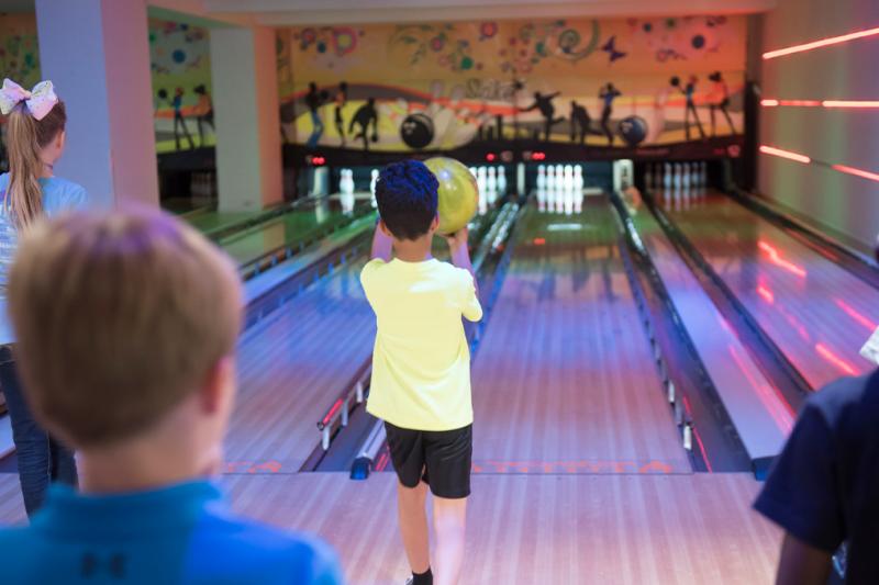 Children watching friend bowl on ten pin bowling lane