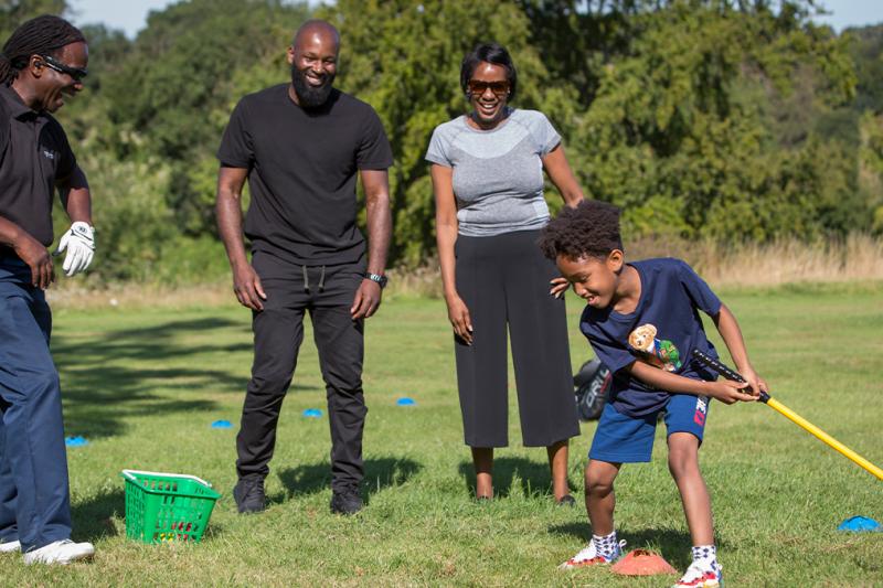 Family playing golf with child hitting ball