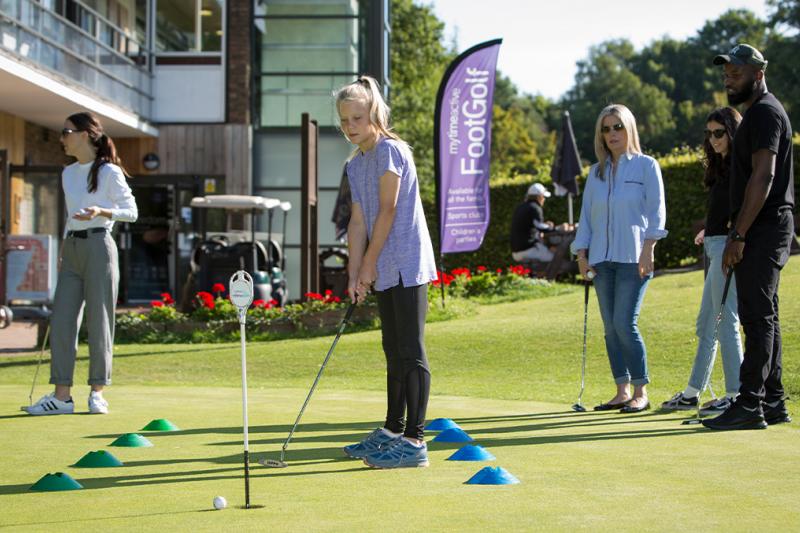 A golf lesson where people are watching a girl putt on the green