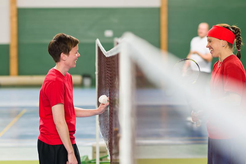 Two people playing badminton talking at the net