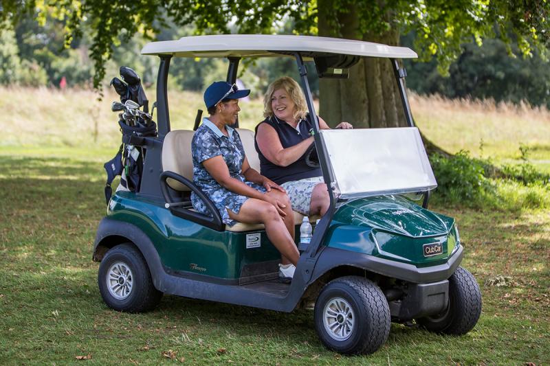 Two ladies playing golf driving a golf buggy